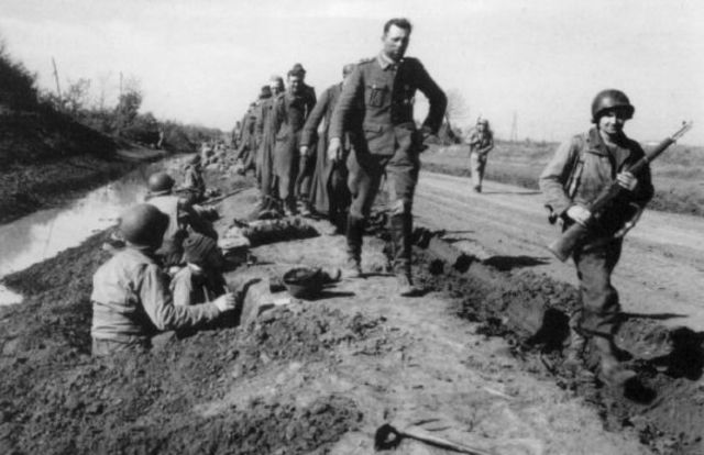 Columna de prisioneros alemanes pasa junto a infantería estadounidense atrincherada junto a un canal de riego